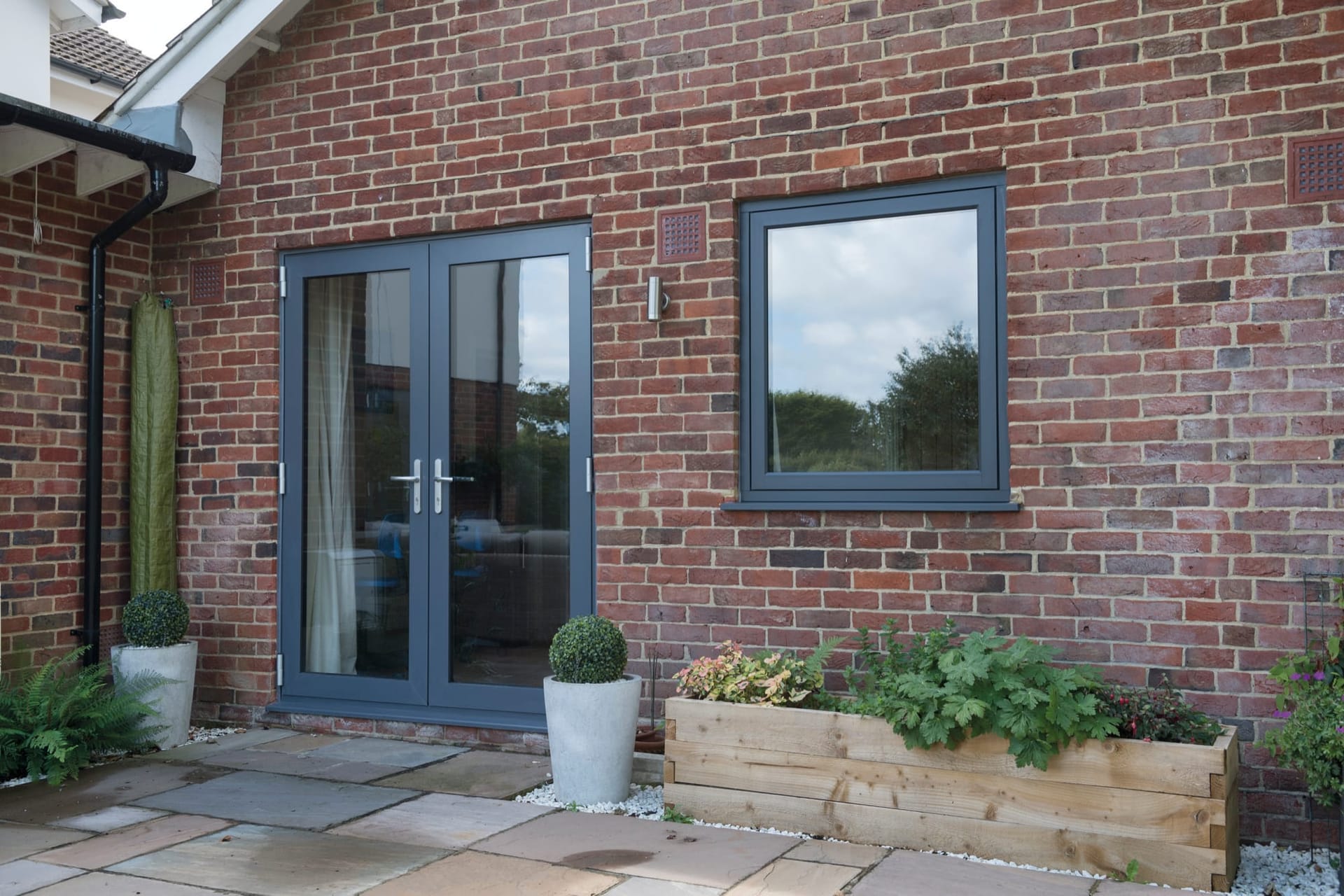 Anthracite grey French doors and a matching casement window on a red brick home