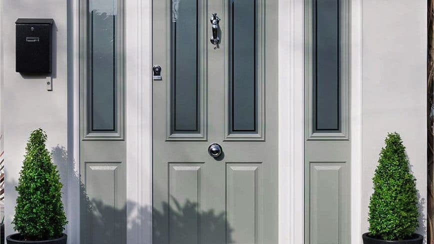 Green composite front door with glazed side panels and clipped topiary either side