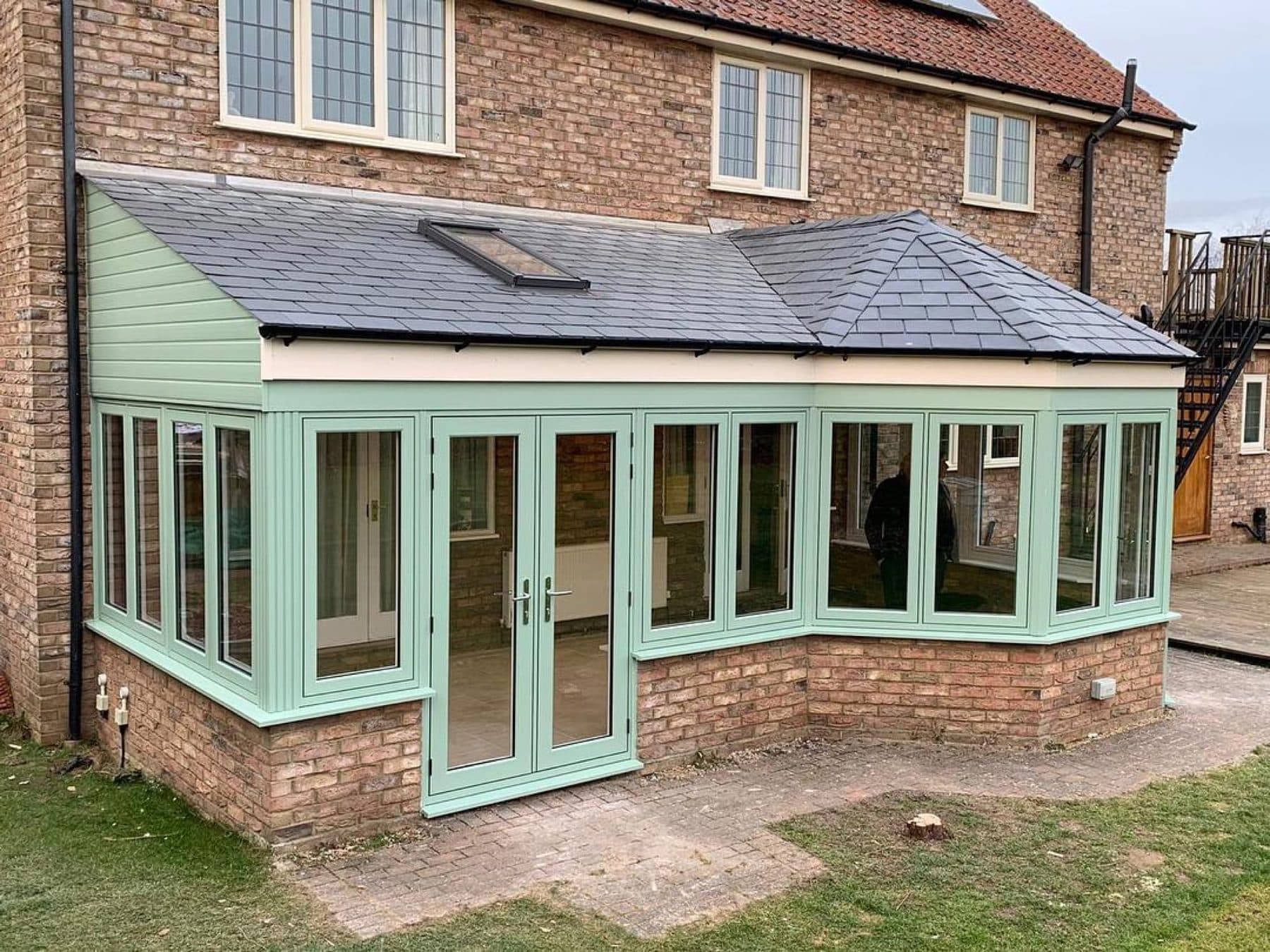 Sage green orangery with a solid tiled roof on a country home
